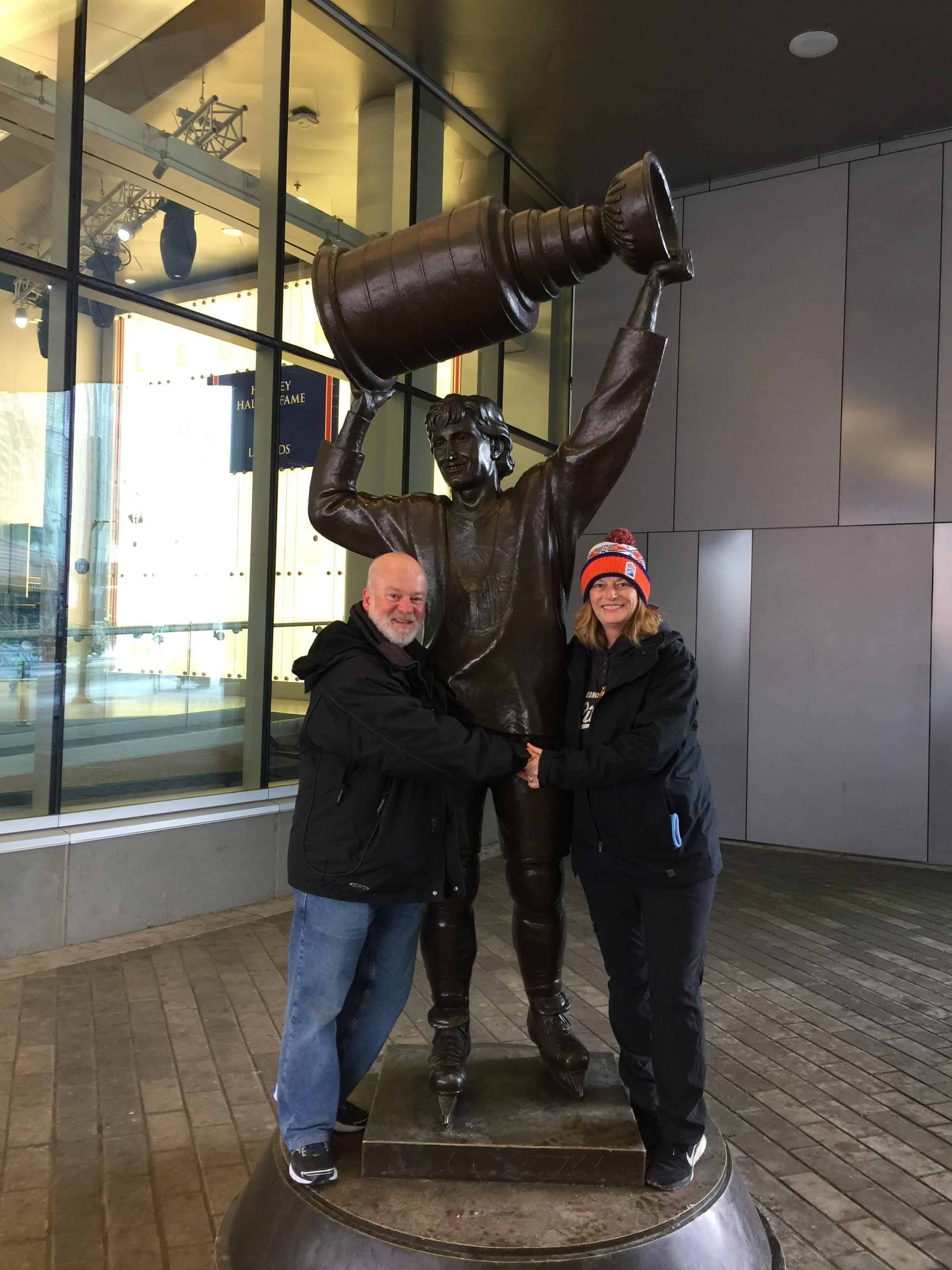 Gail and Paul in 2017 in front of Rogers arena posing with the Gretzky Statue - Hockey Season Edmonton